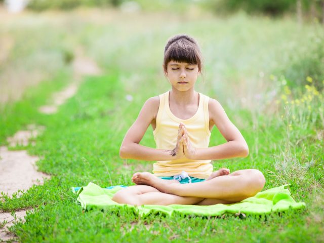 Little girl meditating while sitting in lotus position on grass. Little girl meditating while sitting in lotus position on grass.